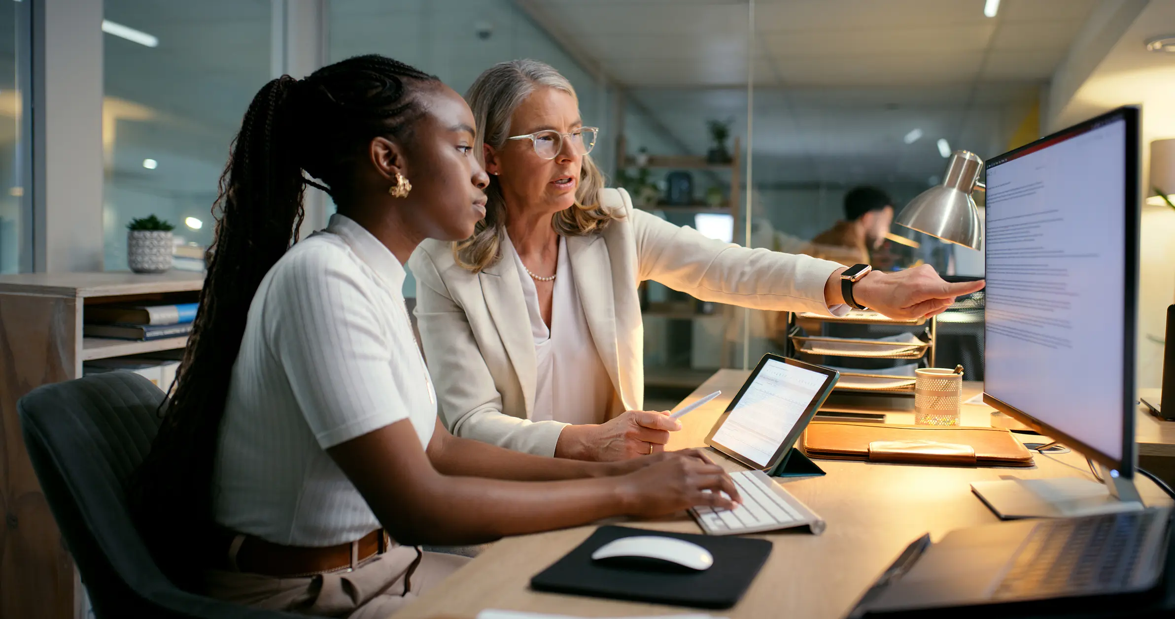 Mentor/manager helping intern accountant to track financial payments at a desk.